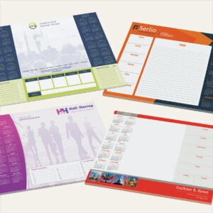 Four promotional a2 printed desk pads on a grey background